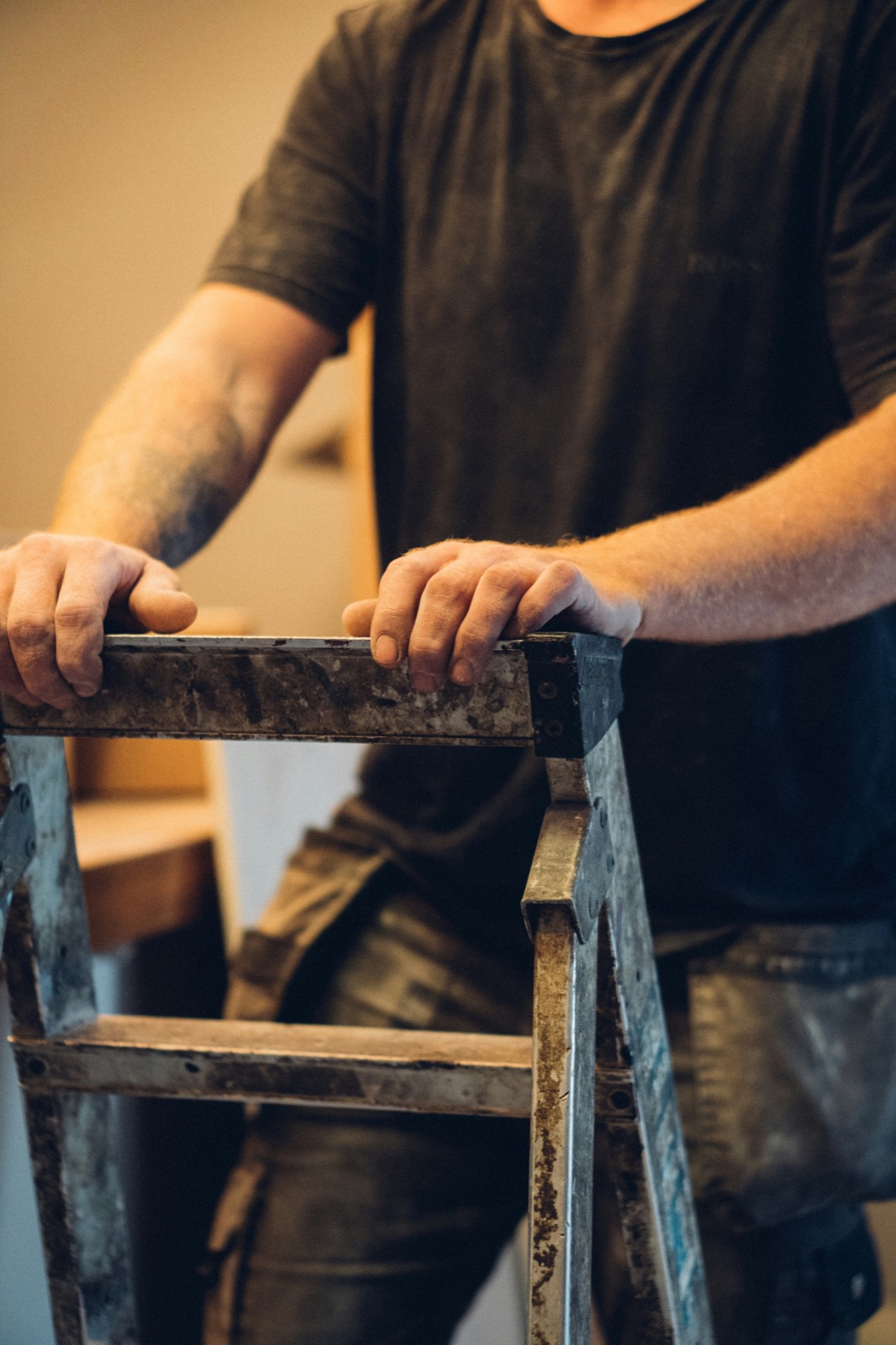 A tradesman's hands gripping a well-used ladder — ready to work